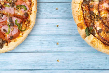 Two different delicious big pizzas on a blue wooden background.