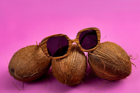 three whole coconuts and wooden glasses on a pink background.の写真素材