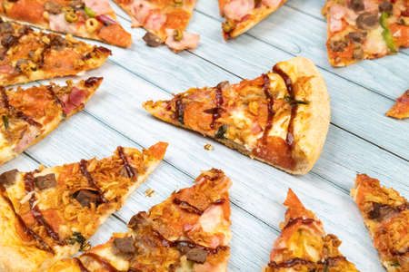 Lots of delicious triangular pizza slices on a blue wooden background