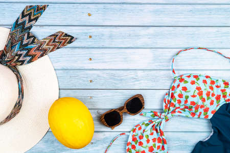 Top view of a straw white hat with glasses and a swimsuit, lying on a blue wooden background.Summer...