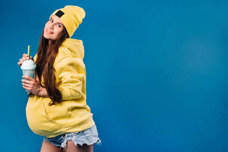 pregnant girl in yellow clothes with a glass of juice on a blue background.の写真素材