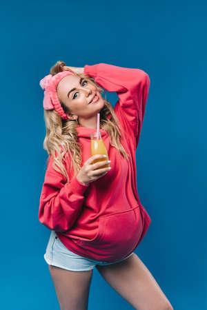 pregnant girl in pink clothes with a bottle of juice on a blue background.の写真素材