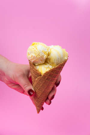 A hand holds an ice cream cone on a pink popsicle background in a waffle cup