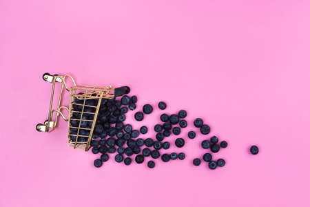 Blueberries in a grocery cart on a pink background. Scattered blueberries near a grocery cart on a pink backgroundの写真素材