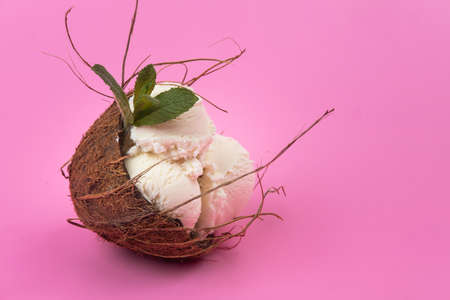 Vanilla ice cream balls in an empty coconut decorated with mint leaves on a pink background.の写真素材