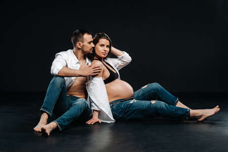 a pregnant woman and a man in a white shirt and jeans in a studio on a black background.の写真素材