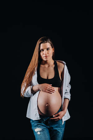 pregnant woman in white shirt and jeans in studio on black backgroundの写真素材