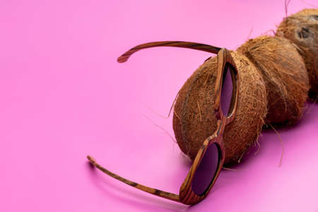 three whole coconuts and wooden glasses on a pink background.の写真素材