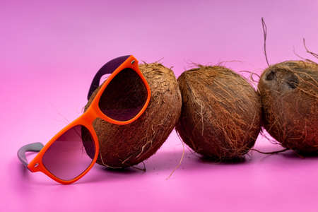 three whole coconuts and orange glasses on a pink background.の写真素材
