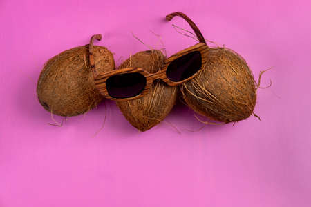 three whole coconuts and wooden glasses on a pink background.の写真素材