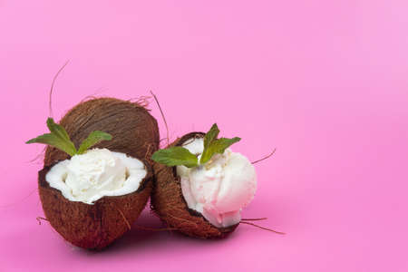 Vanilla ice cream balls in fresh coconut halves decorated with mint leaves on a pink background.の写真素材