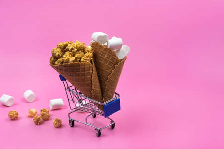 Shopping cart with ice cream cones with sweets on a pink background.