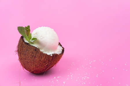 Vanilla ice cream balls in fresh coconut halves, decorated with mint leaves on a pink background.の写真素材