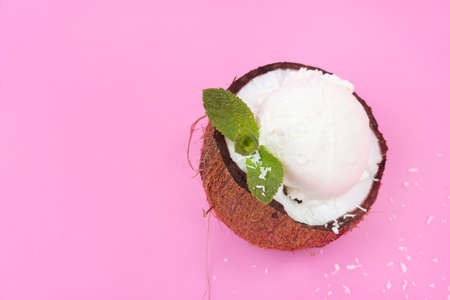 Vanilla ice cream balls in fresh coconut halves, decorated with mint leaves on a pink background.の写真素材