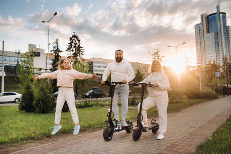 A family in white clothes stands in the city on electric scooters at sunset.