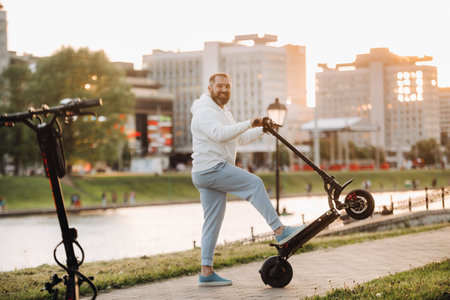 A man with a beard in white clothes rides around the city on an electric scooter at sunset.の写真素材
