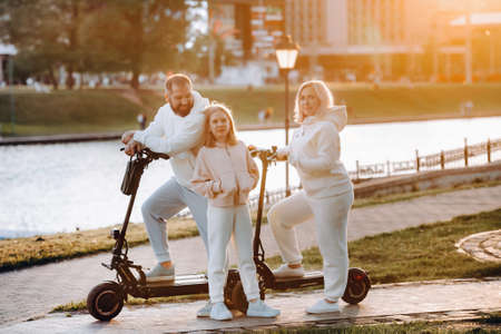 A family in white clothes stands in the city on electric scooters at sunset.の写真素材