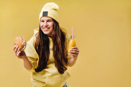 pregnant girl in yellow clothes with hamburgers in her hands on a yellow backgroundの写真素材