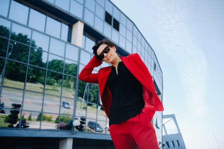 A girl in a red suit stands against the background of a modern building in the city.の写真素材