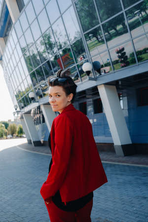 A girl in a red suit stands against the background of a modern building in the city.の写真素材