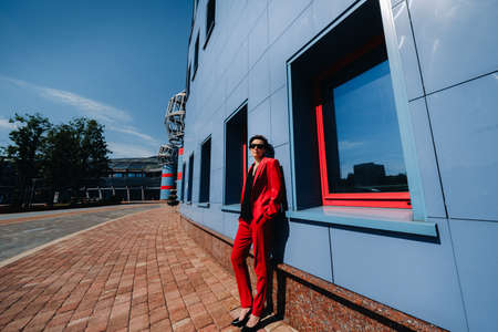 A girl in a red suit stands against the background of a modern building in the city.の写真素材