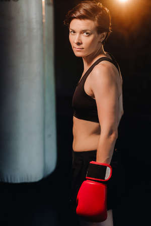 portrait of a female boxer in red gloves in the gym during training.