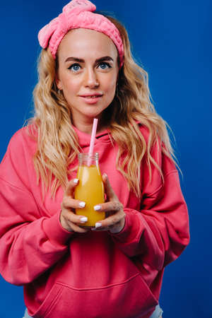 pregnant girl in pink clothes with a bottle of juice on a blue background