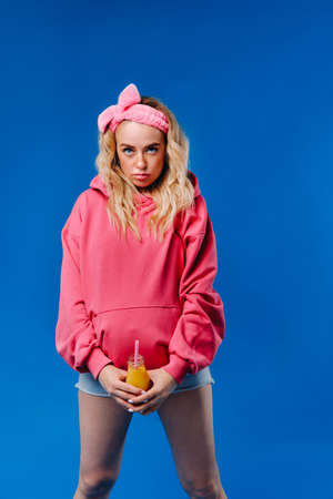 pregnant girl in pink clothes with a bottle of juice on a blue background.の写真素材