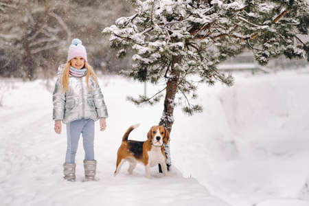 A little girl on a walk with her dog in the winter forest. the owner and the dog are playing in the snow-covered forest.の写真素材