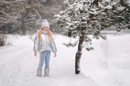 a little girl in a silver jacket in winter goes outside in winter.の写真素材