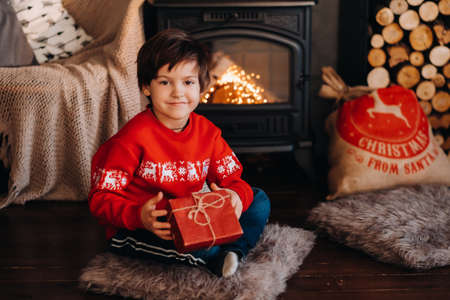 portrait of a smiling boy with a gift in his hands near the fireplace at home.の写真素材