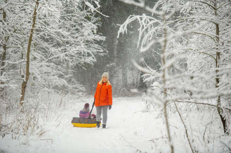 Family mom and daughter in winter with an inflatable circle walk through the snow-covered forest.の写真素材