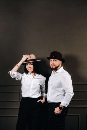 A man and a woman in white shirts and hats on a black background. A couple in love poses in the interior of the studio.の写真素材