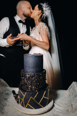 Stylish bride and groom kiss with a cake in their hands in the evening at the wedding.の写真素材