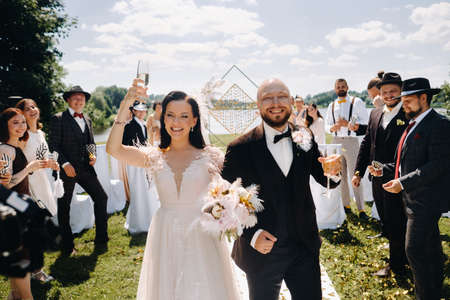 07/08/2021. Nesvizh.Belarus. A happy wedding couple with glasses of wine passes along the guests after the wedding ceremony.のeditorial素材