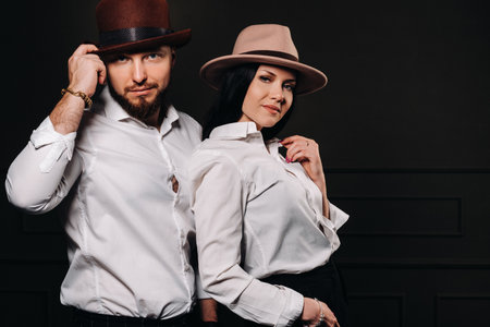 A man and a woman in white shirts and hats on a black background. A couple in love poses in the interior of the studio.の写真素材