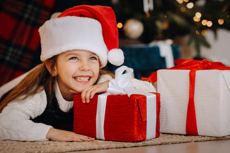 A happy little girl in a Santa Claus hat smiles with gifts in her hands.の写真素材
