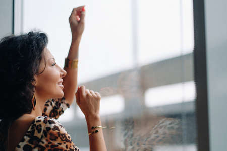 a brunette woman in a tiger dress stands near a large window.