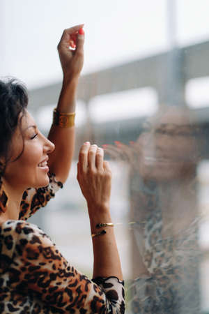 a brunette woman in a tiger dress stands near a large window.の写真素材