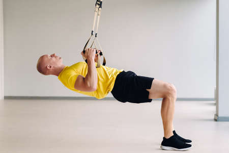 A focused male athlete performing an exercise on functional loops in the gym.の写真素材