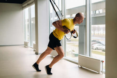 A focused male athlete performing an exercise on functional loops in the gym.