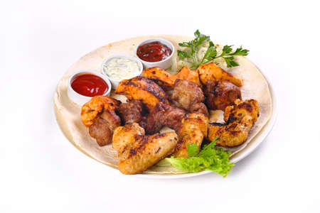 assorted meat on pita bread with vegetables and sauces on a white plate on a white isolated background.の写真素材