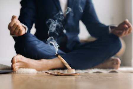 A man in a formal suit meditates while sitting in a fitness room.の写真素材