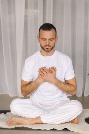 a man in white sportswear is doing yoga with a fitness room. the concept of a healthy lifestyle.