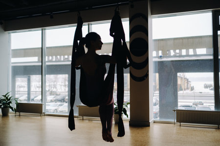 The girl is sitting in a hanging hammock and doing yoga in the gym.の写真素材