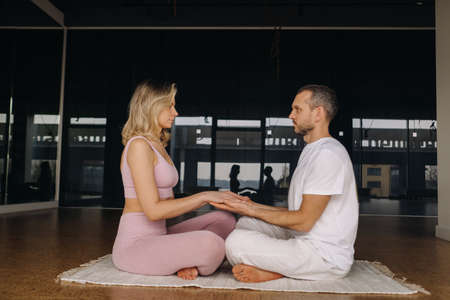 a woman and a man are engaged in pair meditation holding hands in the gymの写真素材