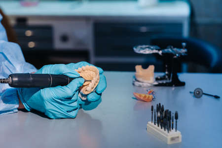 A masked and gloved dental technician works on a prosthetic tooth in his lab.の写真素材