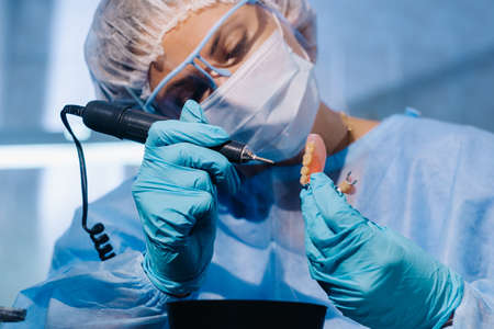 A dental technician in protective clothing is working on a prosthetic tooth in his laboratoryの写真素材