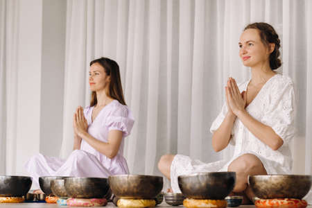Two women are sitting with Tibetan bowls in the lotus position before a yoga class in the gymの写真素材