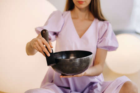 Portrait of a female yoga teacher playing a Tibetan bowl or singing a bell in the gym during a yoga retreat.の写真素材